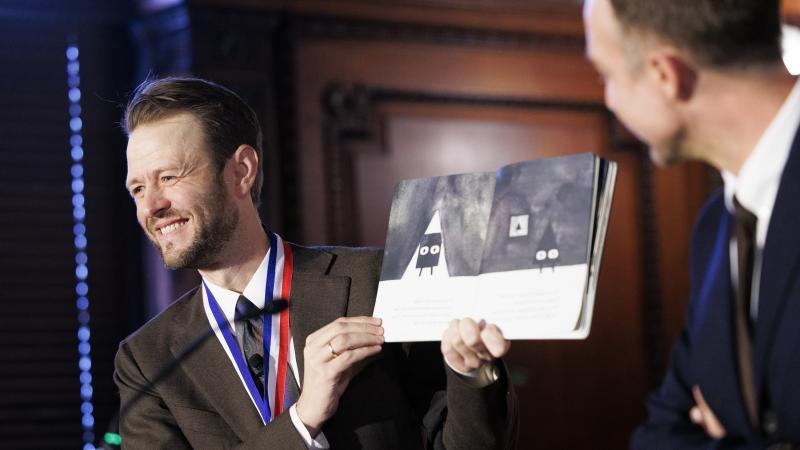 Mac Barnett on stage holding one of his picture books